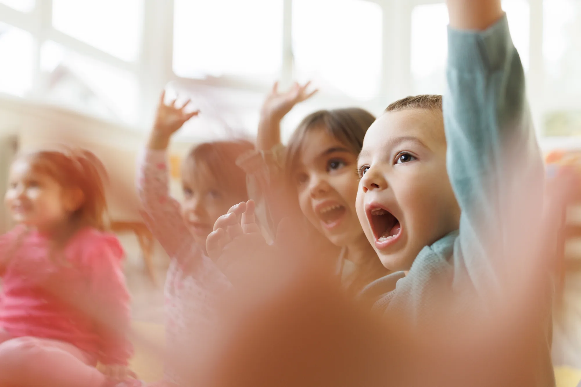 Preschool children with their hands raised, laughing