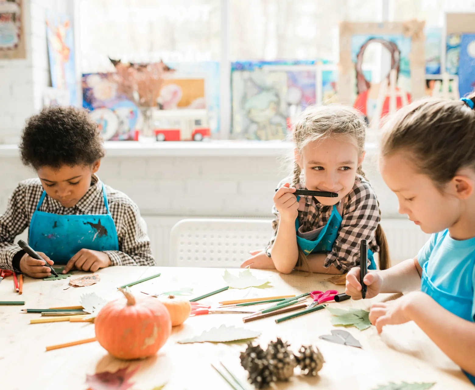 Preschoolers drawing and exploring pumpkins, pine cones and leaves at a craft table