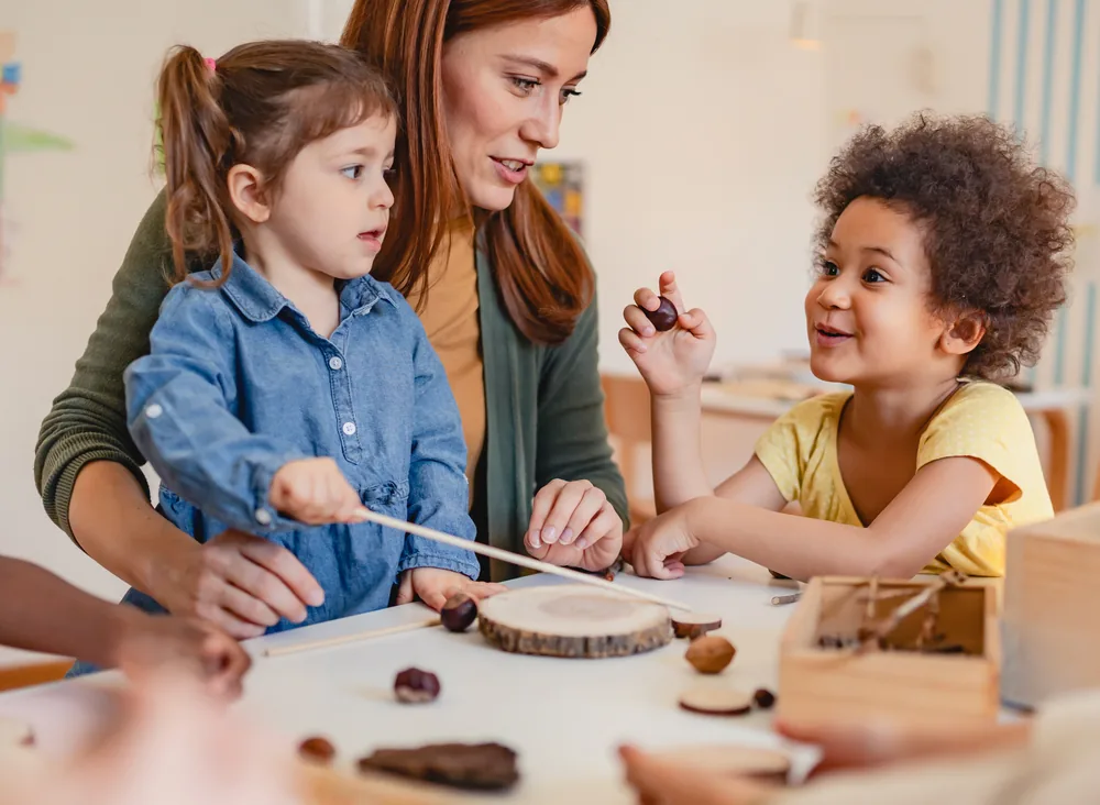 An educator and two children exploring natural materials at a table